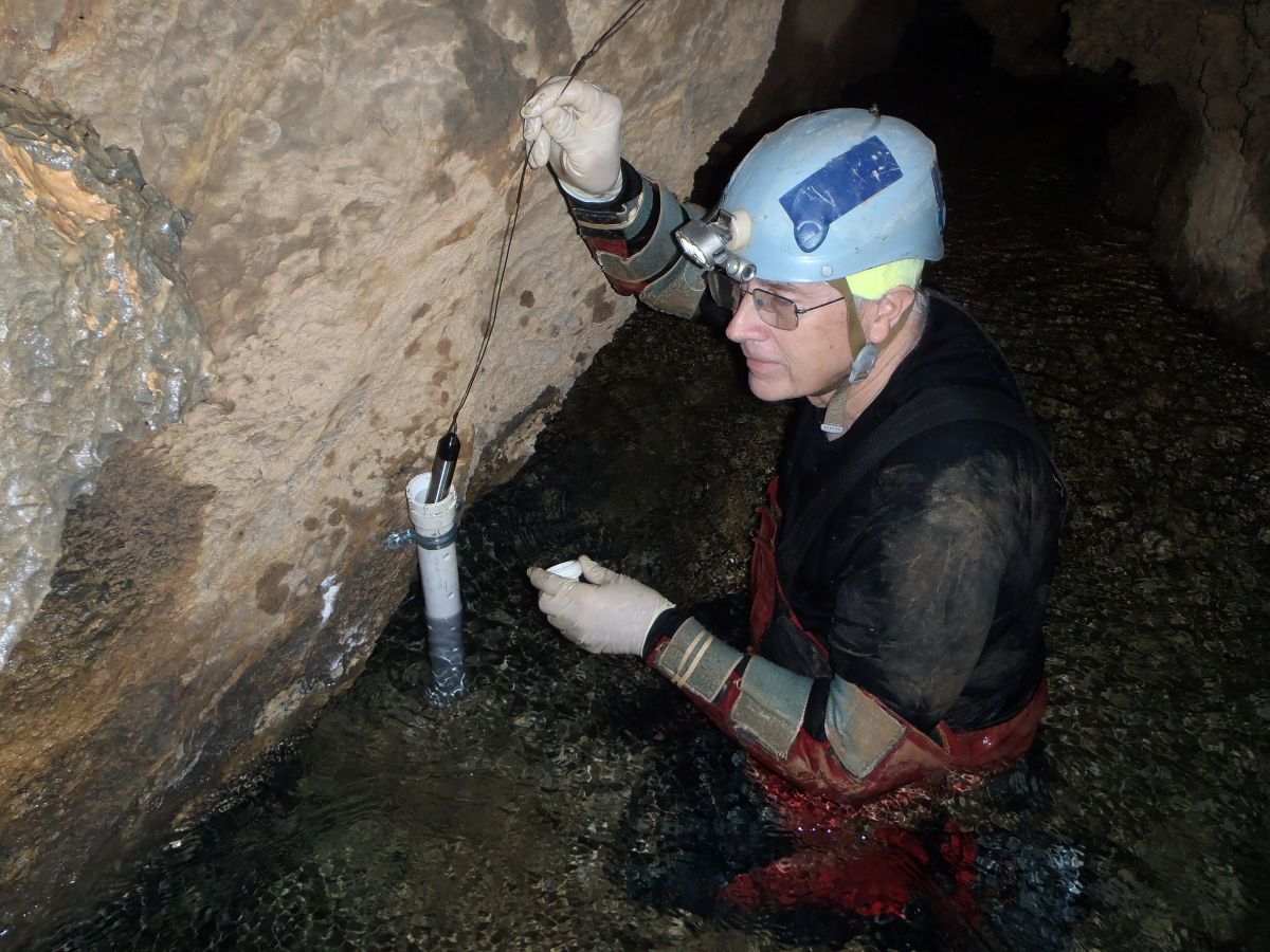 Caver wearing a helmet and gloves installs water pressure device in a body of water inside a cave.